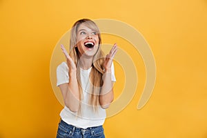 Happy young excited shocked blonde woman posing isolated over yellow wall background