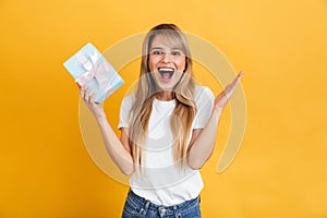 Happy young excited shocked blonde woman posing isolated over yellow wall background holding present gift box