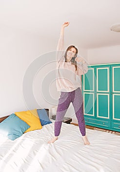 Happy young excited woman dancing on the bed at home