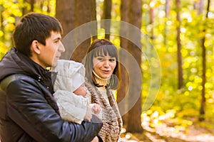 Happy young family in the autumn park outdoors on a sunny day. Mother, father and their little baby boy are walking in