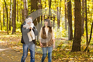 Happy young family in the autumn park outdoors on a sunny day. Mother, father and their little baby boy are walking in