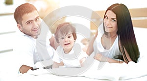 Happy young family with a baby lying in bed and smiling