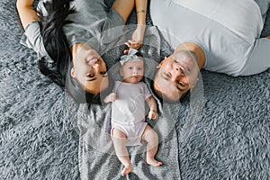 A happy young family with a baby are lying on the bed and smiling. Top view