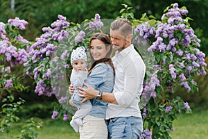 Happy young family with a baby are relaxing in the spring blooming lilac park