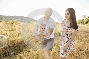 Happy young family with baby son playing and having fun together in nature on field