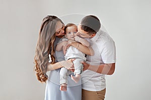 Happy young family. Beautiful Mother and father kissing their baby. Portrait of Mom, dad and smiling child on hands