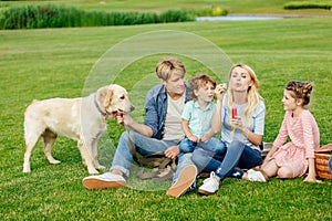 happy young family blowing soap bubbles while resting with dog