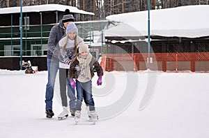 Happy young family with child skate at the outdoor ice rink in the winter. Beautiful family walking and playing on the ice in