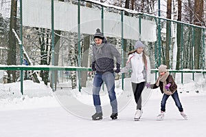 Happy young family with child skate at the outdoor ice rink in the winter. Beautiful family walking and playing on the ice in