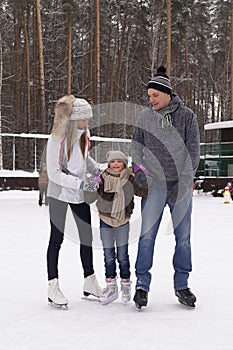 Happy young family with child skate at the outdoor ice rink in the winter. Beautiful family walking and playing on the ice in