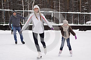 Happy young family with child skate at the outdoor ice rink in the winter. Beautiful family walking and playing on the ice in
