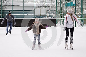 Happy young family with child skate at the outdoor ice rink in the winter. Beautiful family walking and playing on the ice in