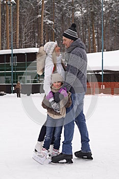 Happy young family with child skate at the outdoor ice rink in the winter. Beautiful family walking and playing on the ice in wint