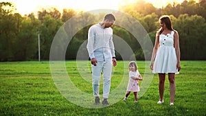 Happy young family with child walking on summer field. Healthy mother, father and little daughter girl enjoying nature