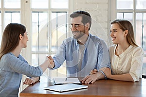 Happy young family couple shaking hands with real estate agent.