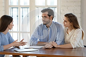 Happy young family couple visiting female real estate agent.