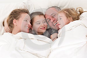 Happy young family cuddling together in bed