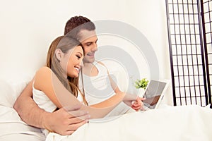 Happy young family doing internet shopping while lying in bed