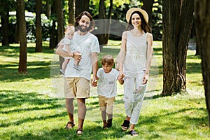 Happy young family dressed in the white casual clothes walks in the park on a sunny summer day.