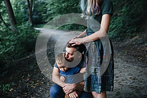 Happy young family father, mother and little son hugging and touching outdoors, playing together in summer park