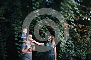 Happy young family father, mother and little son hugging and touching outdoors, playing together in summer park