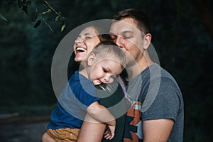 Happy young family father, mother and little son hugging and touching outdoors, playing together in summer park