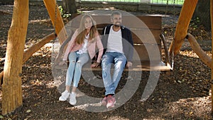 Happy young family father, mother, son and little daughter riding on a swing in the park. Laugh and smile. Children run