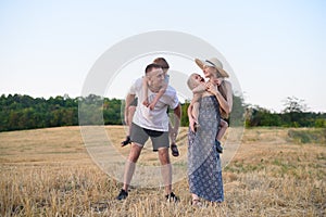 Happy young family. A father, a pregnant mother, and two little sons on their backs. Beveled wheat field on the background. Sunset