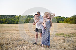 Happy young family. A father, a pregnant mother, and two little sons on their backs. Beveled wheat field on the background. Sunset