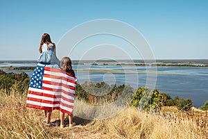 Happy young family with the flag of america in nature on the background of the bay. Free lifestyle. View from the back