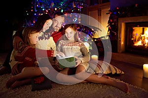 Happy young family of four using a tablet pc at home by a fireplace in warm and cozy living room on Christmas eve