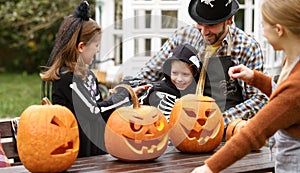 Happy young family in Halloween costumes carving pumpkins together in backyard photo