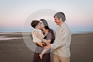 Happy young family have fun on beach hug and kiss at sunset. Family look natural clothes