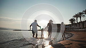 Happy young family have fun walking on beach at sunset. Family silhouette travel holiday.