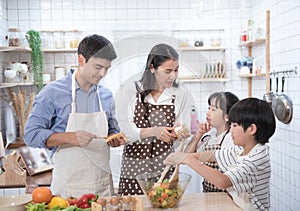 Happy young family have leisure time in kitchen,Father help mother cooking,daughter and son eat yam and bread