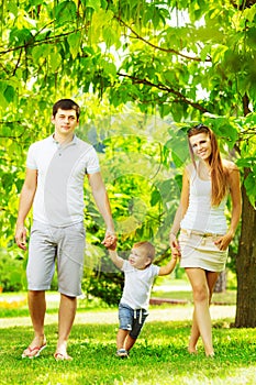 Happy young family is having fun in the green summer park outdoors on a sunny day. Mother, father and their little baby-boy are w