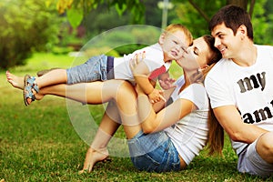 Happy young family is having fun in the green summer park outdoors on a sunny day. Mother, father and their little baby-boy are w