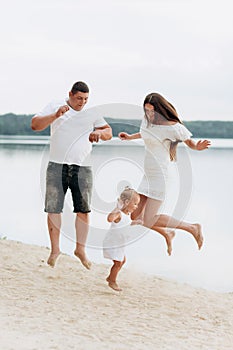Happy young family having fun near the lake, mom dad and daughter playing outdoors. summer holiday, Mother`s, father`s, baby`s