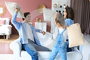 Happy young family having fun with pillows on sofa