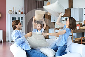 Happy young family having fun with pillows on sofa