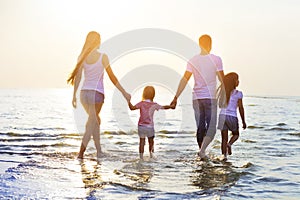 Happy young family having fun running on beach at sunset