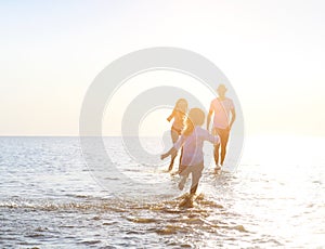 Happy young family having fun running on beach at sunset
