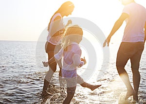 Happy young family having fun running on beach at sunset