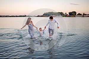 Happy young family having fun running on water at the beach