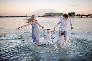 Happy young family having fun running on water at the beach