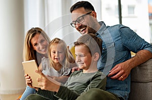 Happy young family having fun time at home. Parents with children using digital device.