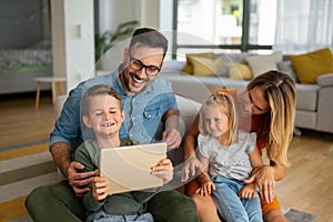 Happy young family having fun time at home. Parents with children using digital device.