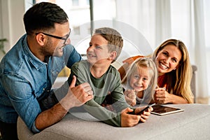 Happy young family having fun time at home. Parents with children using digital device.