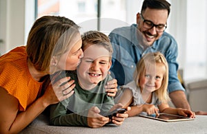 Happy young family having fun time at home. Parents with children using digital device.