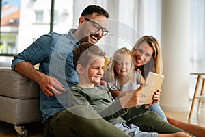 Happy young family having fun time at home. Parents with children using tablet